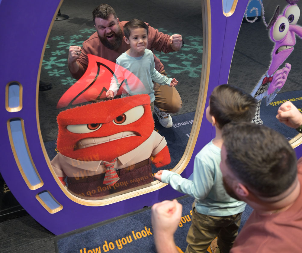 Grown-up and child making angry faces in a mirror with the Anger character from Inside Out.